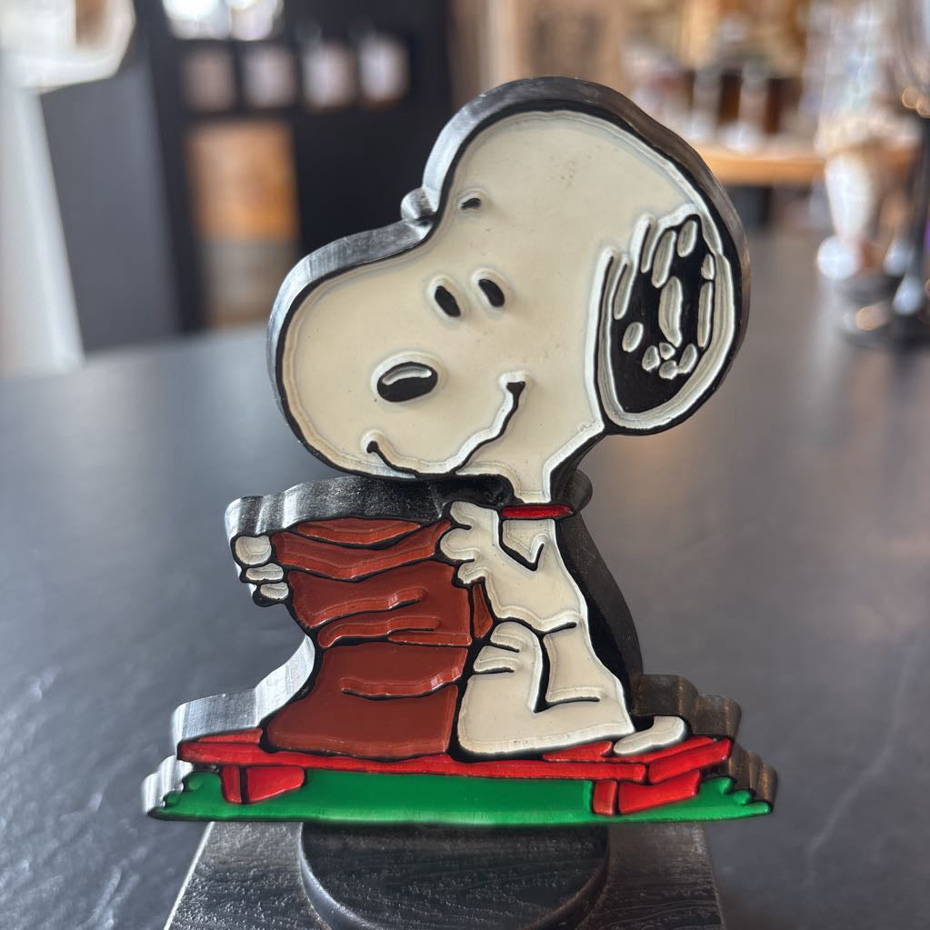 A small figure of snoopy on a pedestal opening up a brown bag 