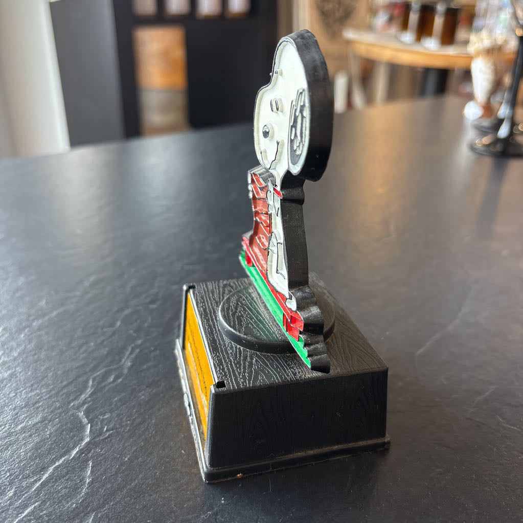 A small figure of snoopy on a pedestal. He's opening up a brown bag and the phrase at the bottom reads, "Life is like a brown bag...full of wonderful surprises!" 