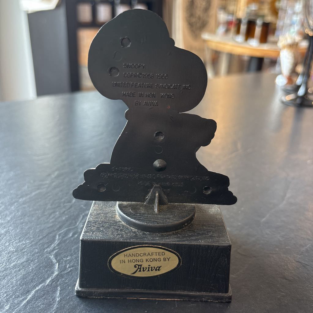 A small figure of snoopy on a pedestal. He's opening up a brown bag and the phrase at the bottom reads, "Life is like a brown bag...full of wonderful surprises!" 