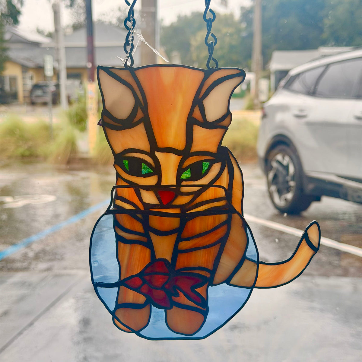 stained glass orange cat looking at fish in bowl hanging on window