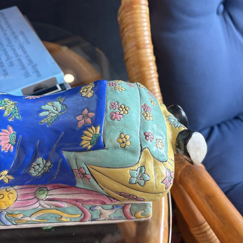 A hand-painted figure of a reclining boy dressed in a vivid royal blue robe adorned with delicate floral motifs and a decorative pedestal base.