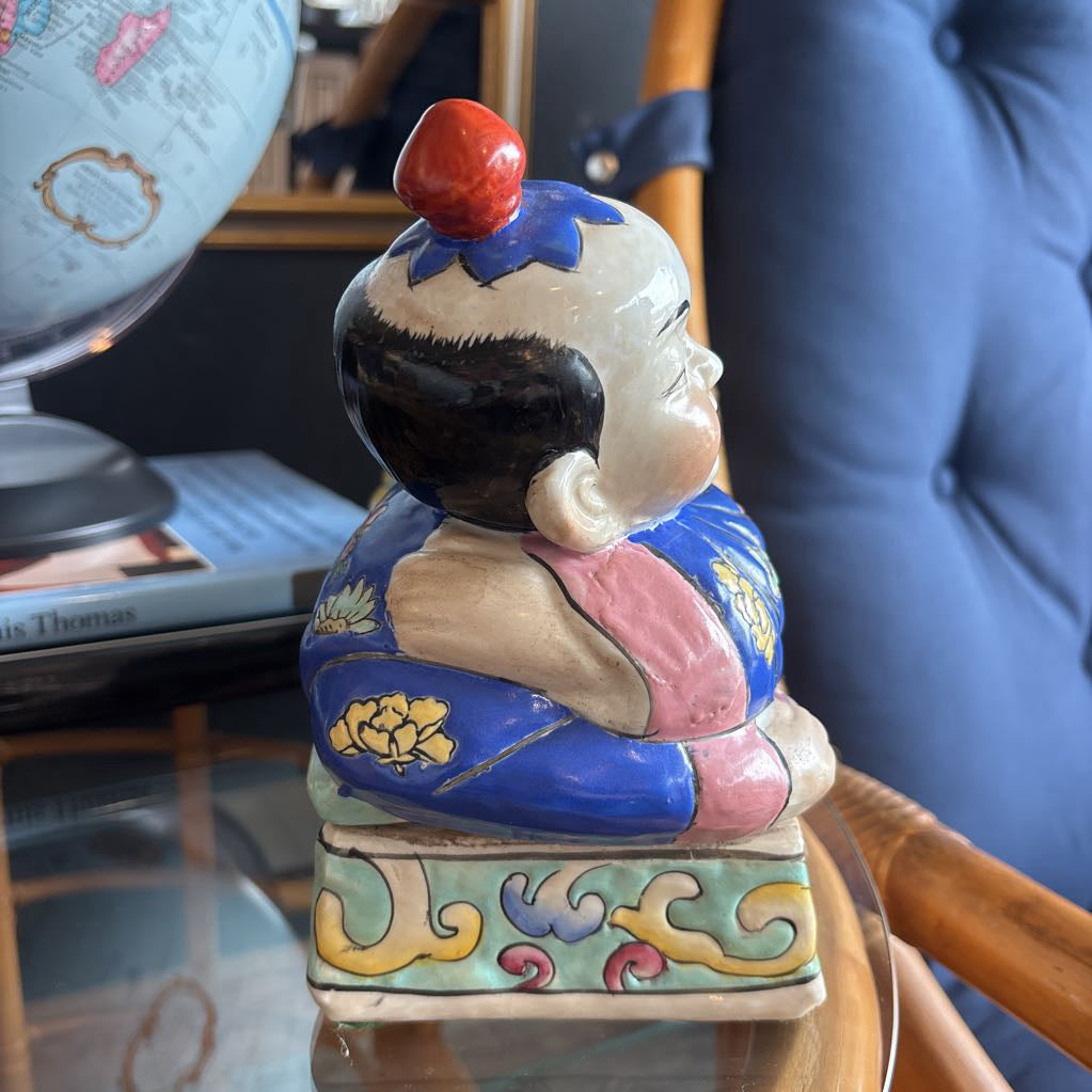 A hand-painted figure of a reclining boy dressed in a vivid royal blue robe adorned with delicate floral motifs and a decorative pedestal base.