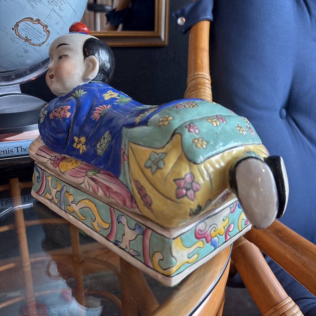 A hand-painted figure of a reclining boy dressed in a vivid royal blue robe adorned with delicate floral motifs and a decorative pedestal base.