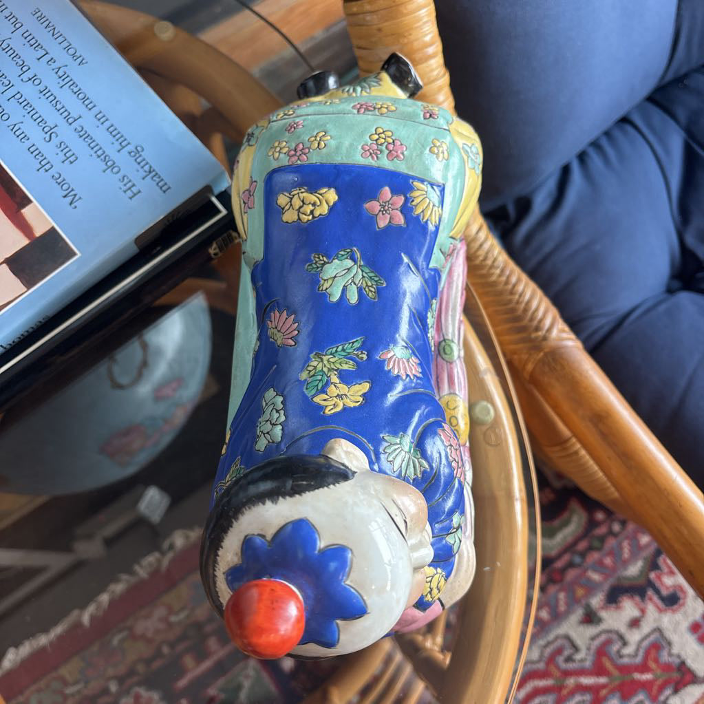 A hand-painted figure of a reclining boy dressed in a vivid royal blue robe adorned with delicate floral motifs and a decorative pedestal base.