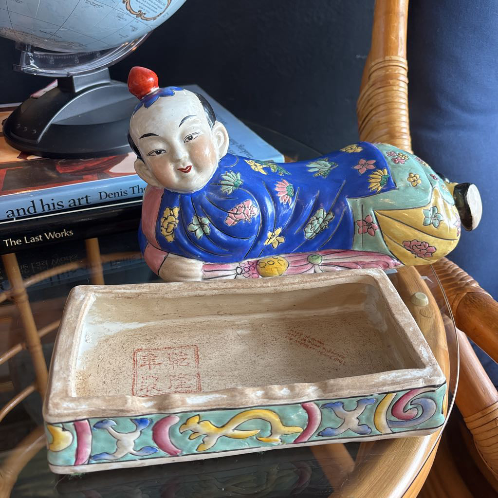 A hand-painted figure of a reclining boy dressed in a vivid royal blue robe adorned with delicate floral motifs and a decorative pedestal base.