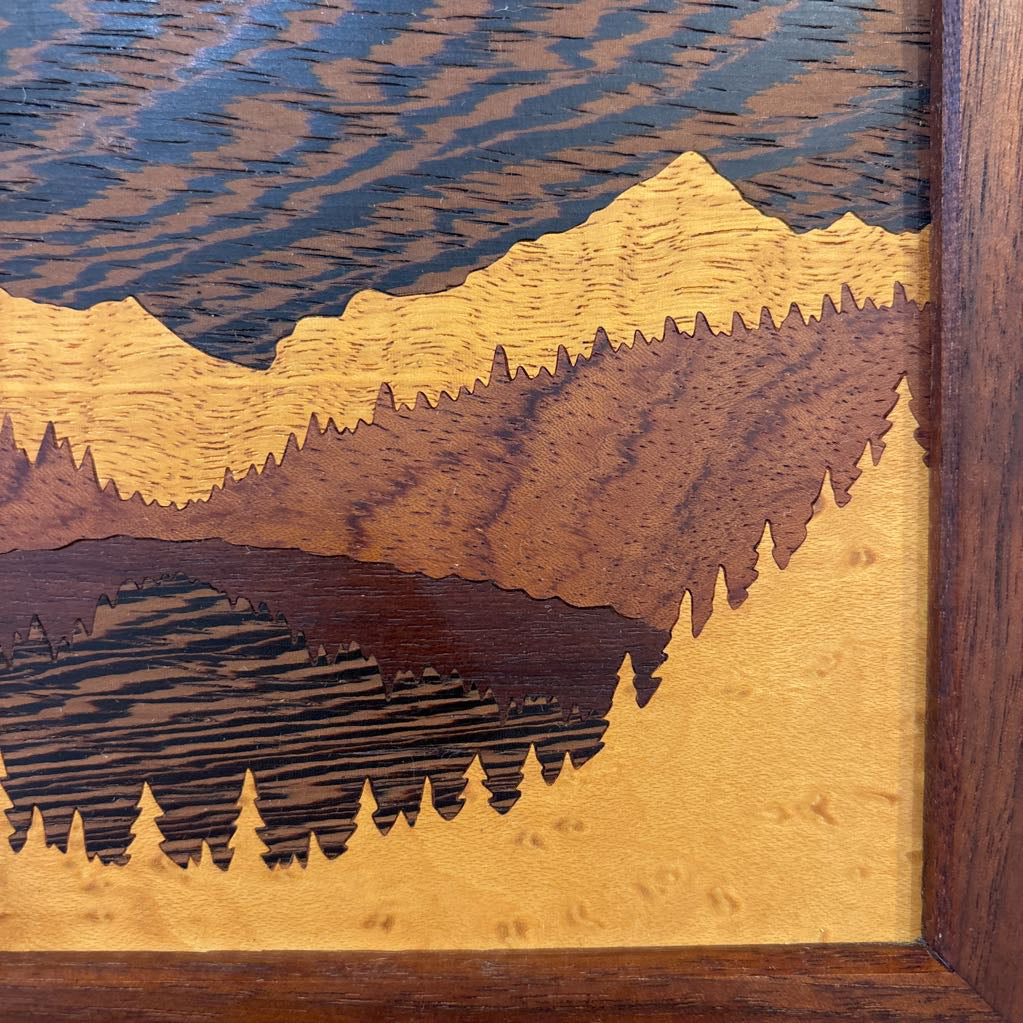 A square framed wooden inlaid artwork of a bird flying over mountains and forests with different colors and textures of wood. 