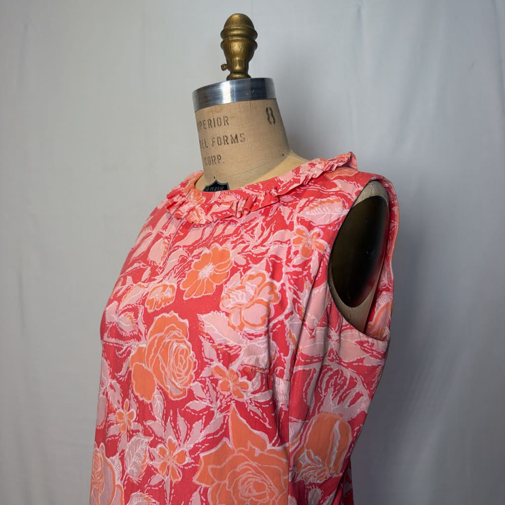 A pink & peach floral mod dress on a dress form in front of a white wall.