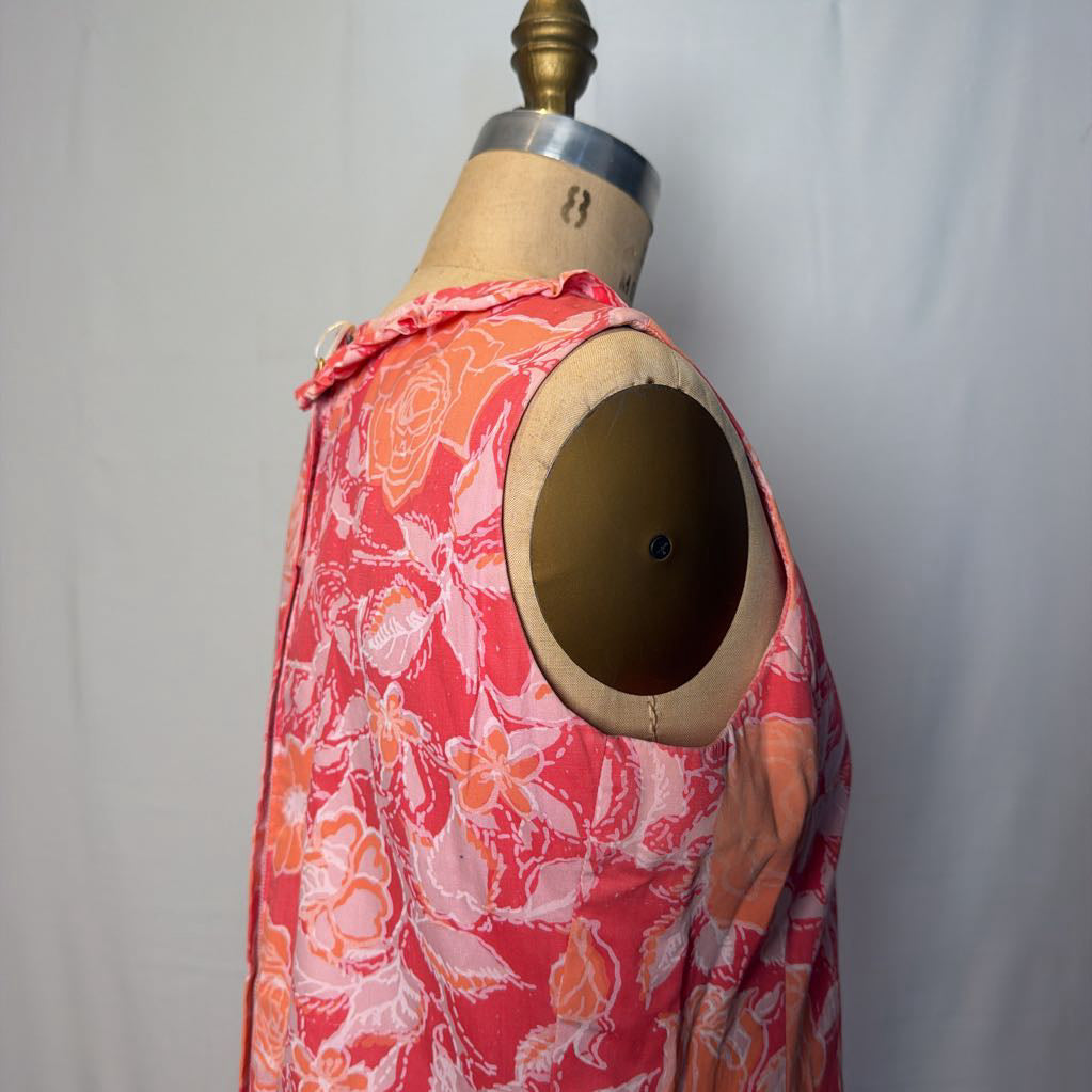 A pink & peach floral mod dress on a dress form in front of a white wall.