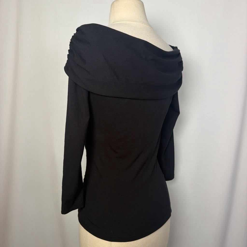 A black top with 3/4 sleeves and a draped collar with a large flower adornment on a mannequin in front of a white wall. 