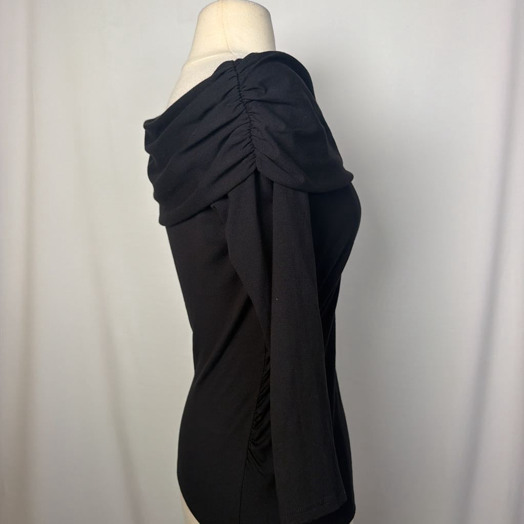 A black top with 3/4 sleeves and a draped collar with a large flower adornment on a mannequin in front of a white wall. 