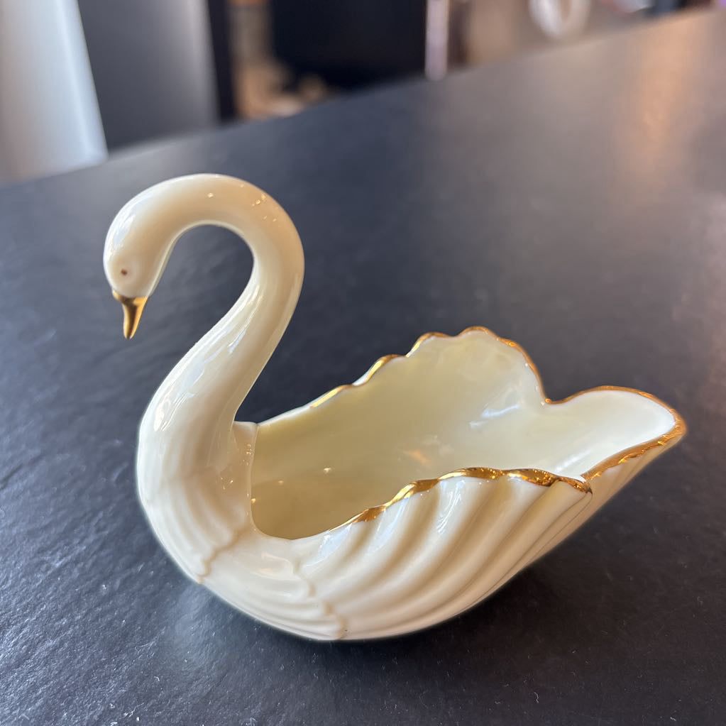 A small ceramic white swan figurine with gold trim on the wings and beak on a dark surface. 