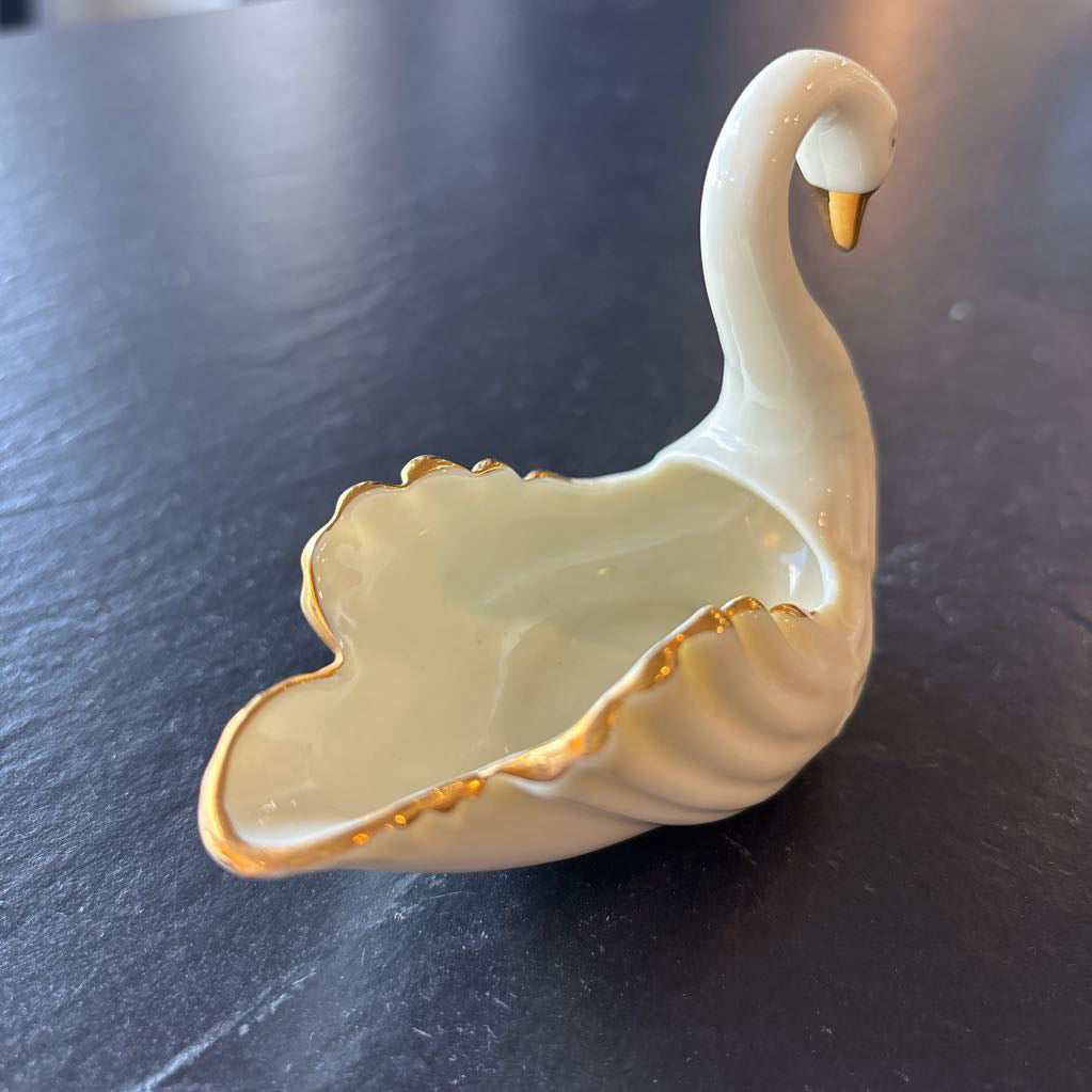 A small ceramic white swan figurine with gold trim on the wings and beak on a dark surface. 