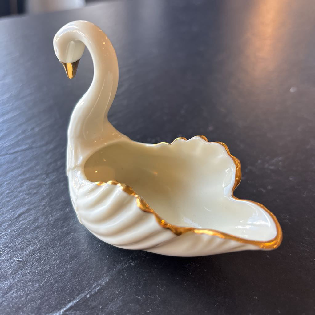 A small ceramic white swan figurine with gold trim on the wings and beak on a dark surface. 