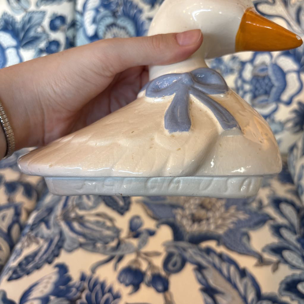 A hand holding the top of a duck shaped cookie jar showing the branding stamps along the lip of the lid. 