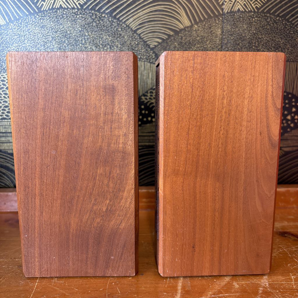 Two wooden bookends sitting on a wooden surface in front of a black and gold wallpaper.