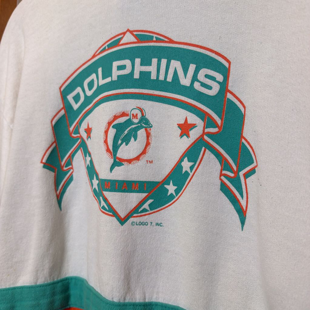 A white, orange, and turquoise Miami Dolphins branded sweatshirt on a wooden rack.  