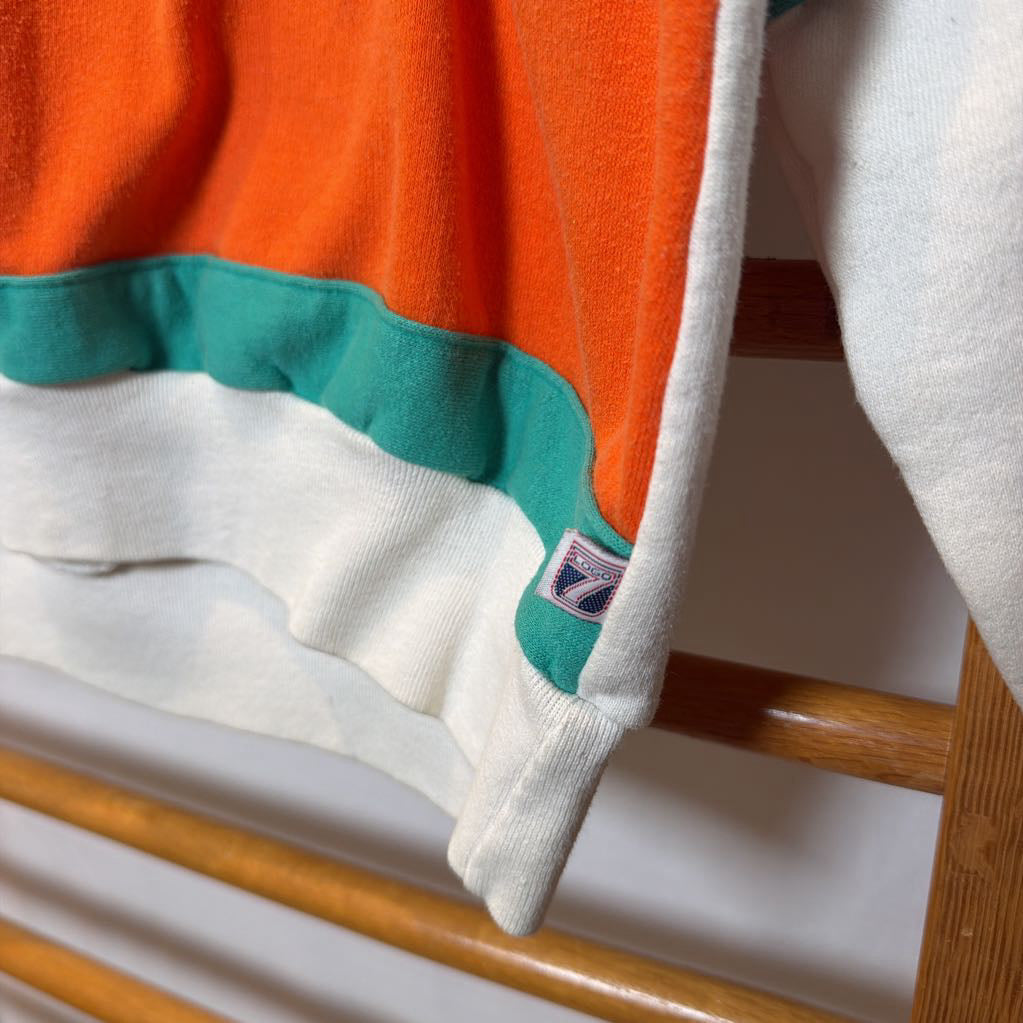 A white, orange, and turquoise Miami Dolphins branded sweatshirt on a wooden rack.  