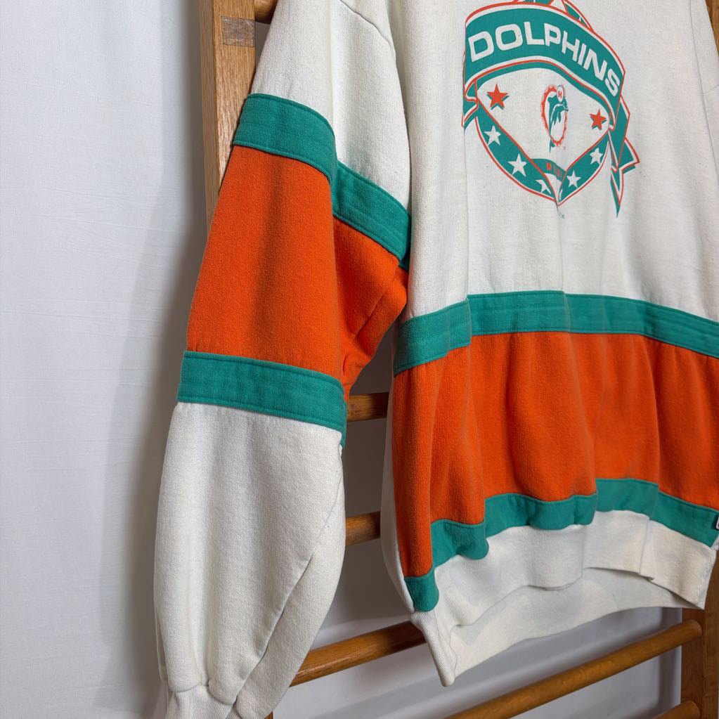 A white, orange, and turquoise Miami Dolphins branded sweatshirt on a wooden rack.  