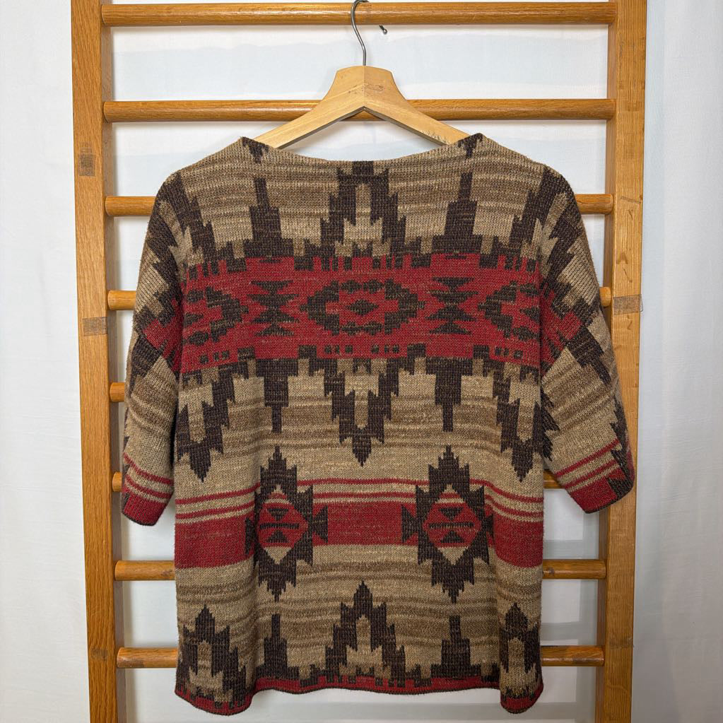 A short sleeve sweater with a tapestry design on a wooden rack. 