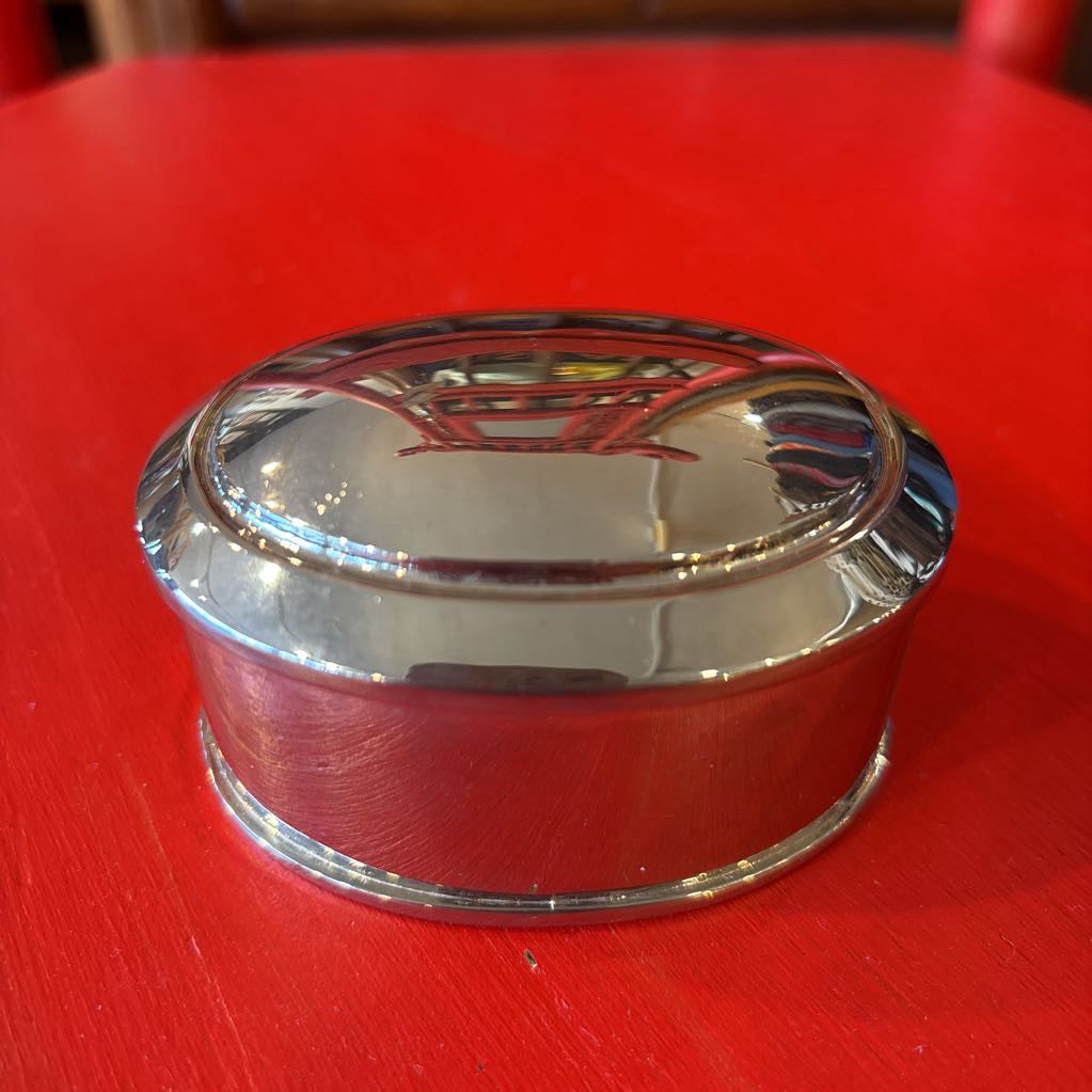 A silver jewelry box reflecting the red surface its on.