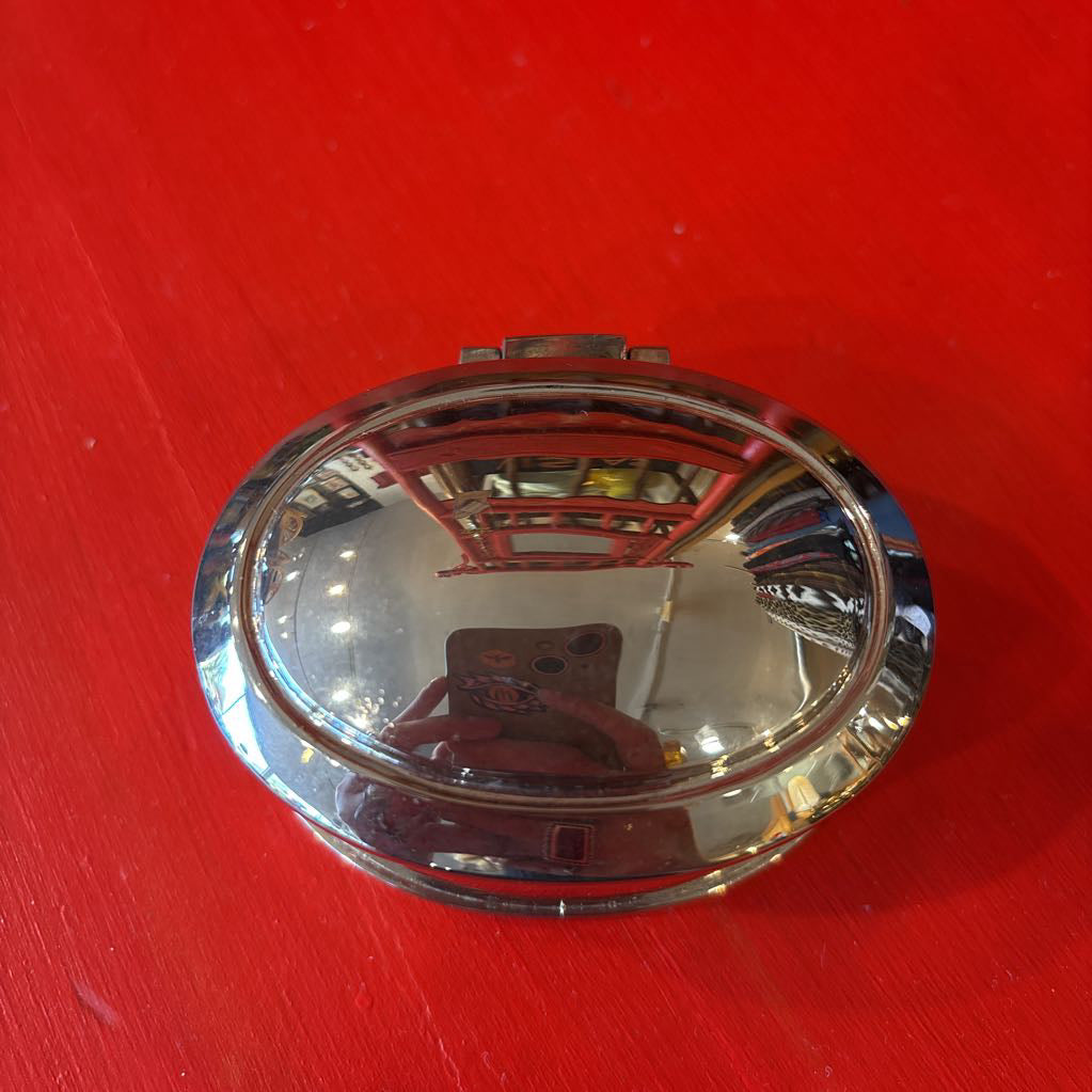 A silver jewelry box on a red surface with the reflection of a camera on the top.