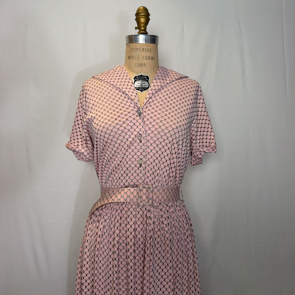 A light pink dress with cuffed sleeves and a belted waist on a mannequin in front of a white wall.