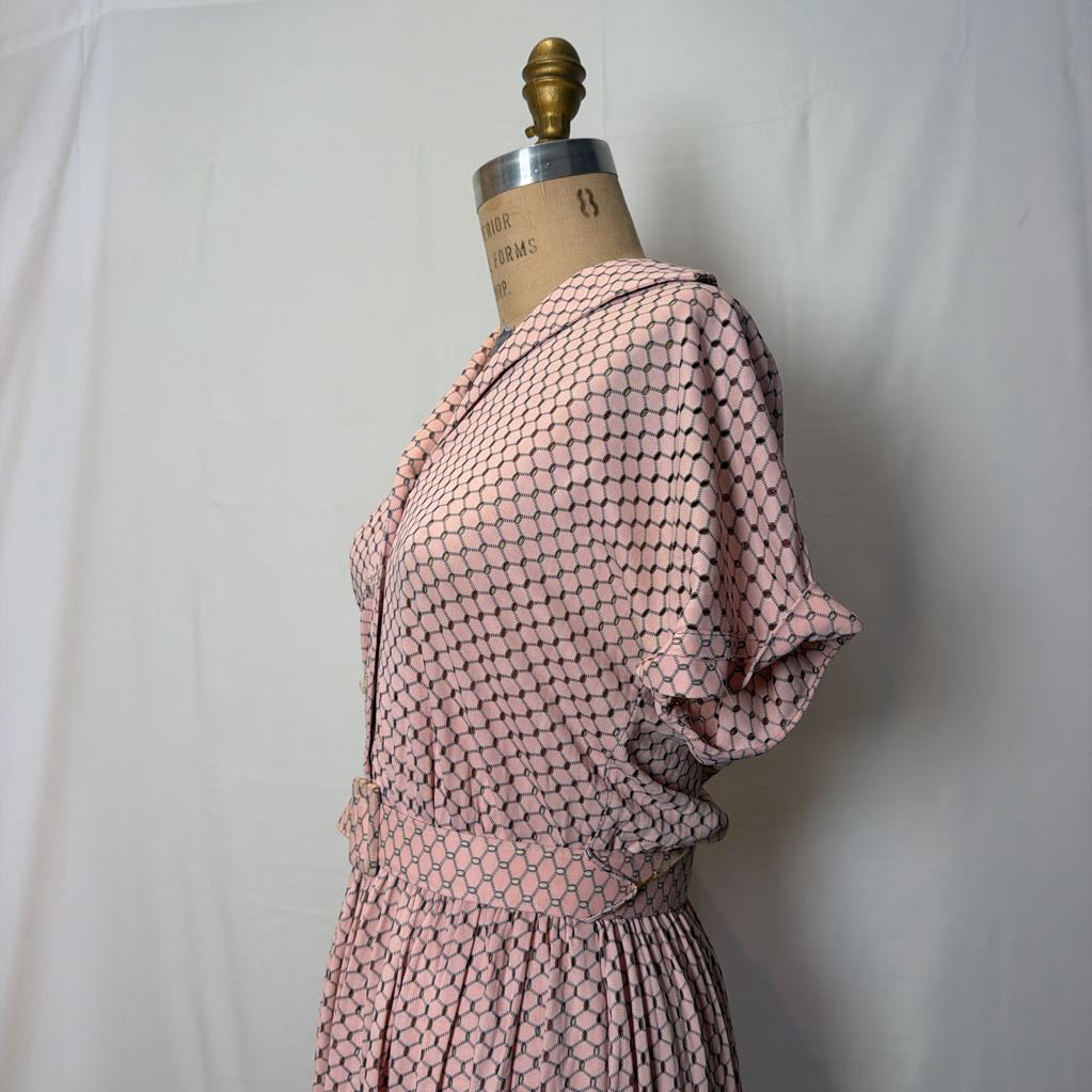A light pink dress with cuffed sleeves and a belted waist on a mannequin in front of a white wall.