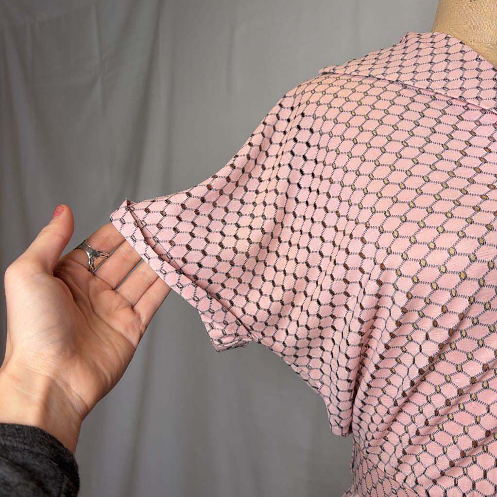 A light pink dress with cuffed sleeves and a belted waist on a mannequin in front of a white wall.