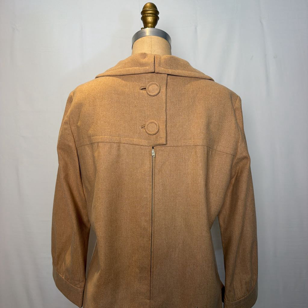A long sleeve tan wool dress on a mannequin in front of a white wall. 