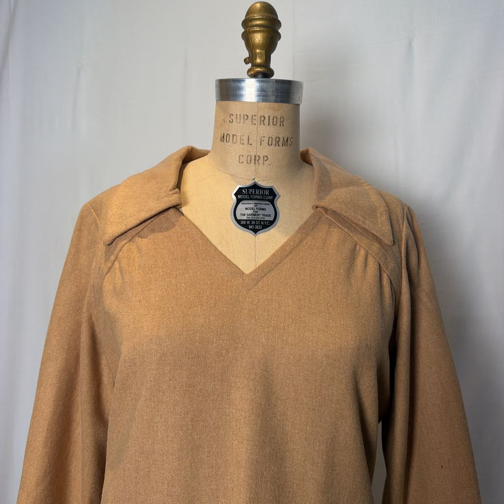 A long sleeve tan wool dress on a mannequin in front of a white wall. 