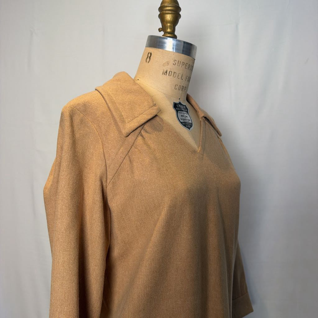 A long sleeve tan wool dress on a mannequin in front of a white wall. 