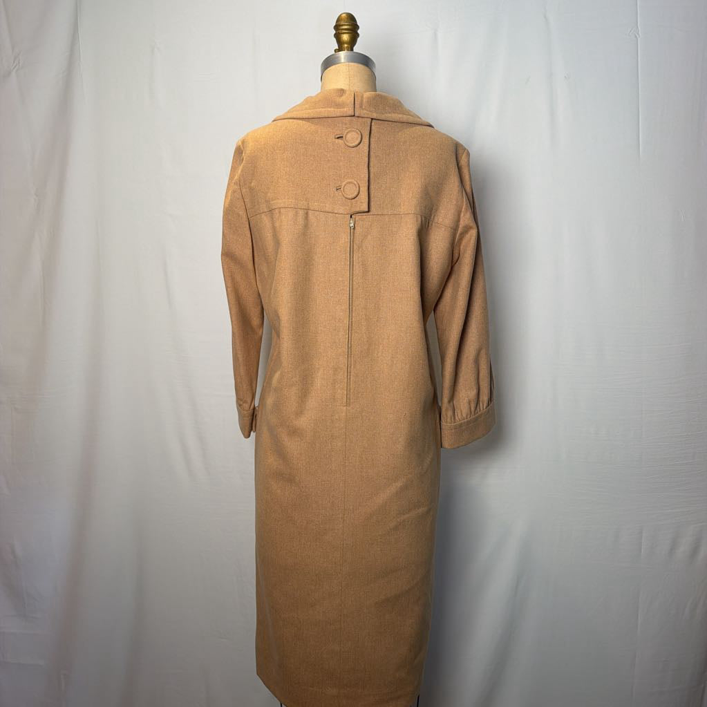 A long sleeve tan wool dress on a mannequin in front of a white wall. 