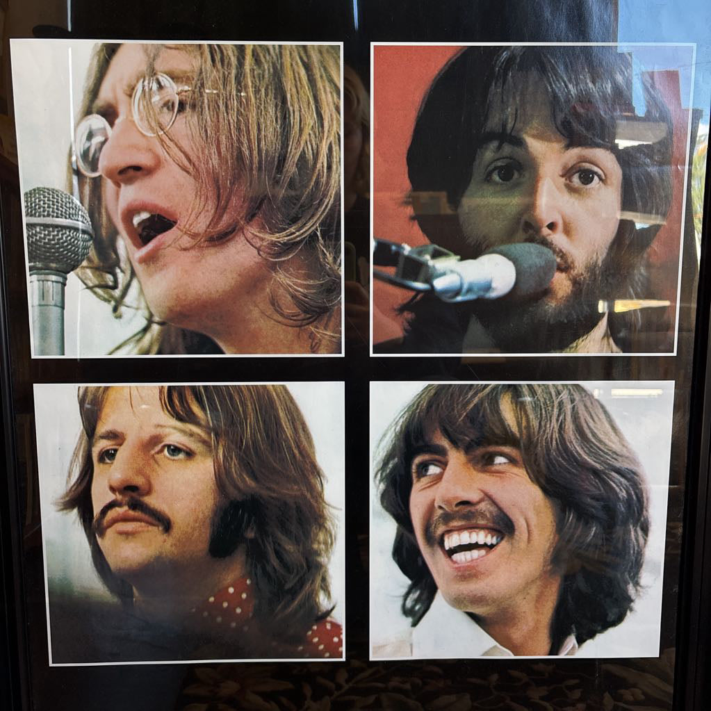A black framed poster of the Beatles' album Let It Be leaning against a bookcase. 