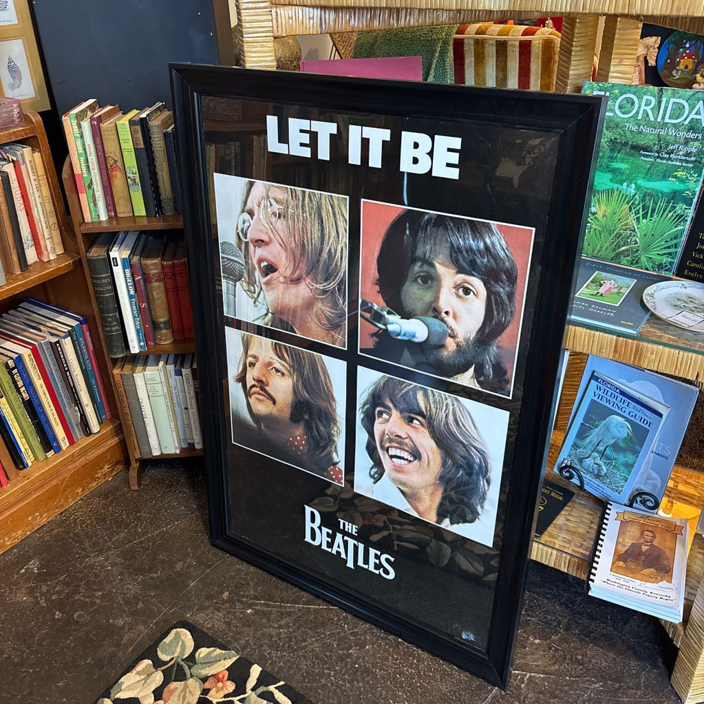 A black framed poster of the Beatles' album Let It Be leaning against a bookcase. 