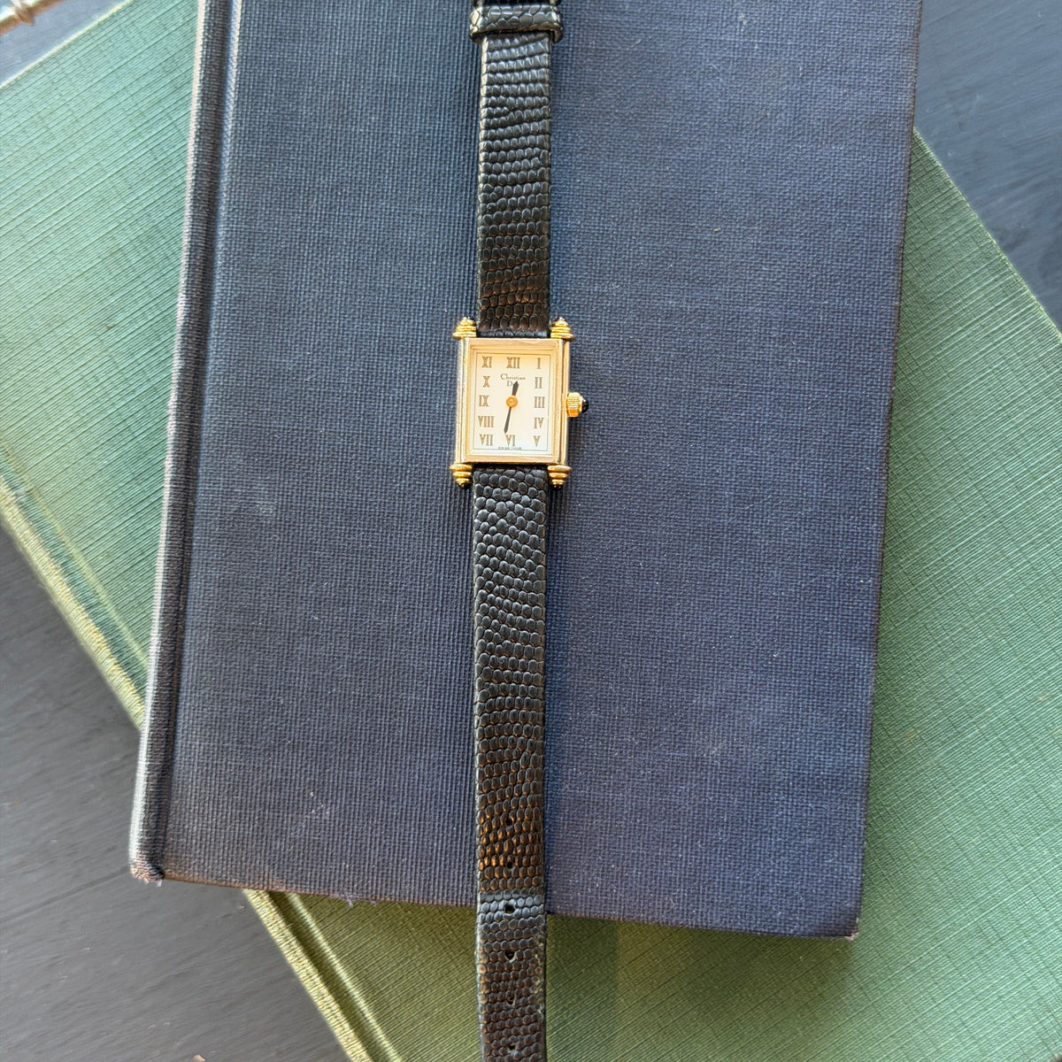 Black Christian Dior Tank Watch sitting on two vintage books