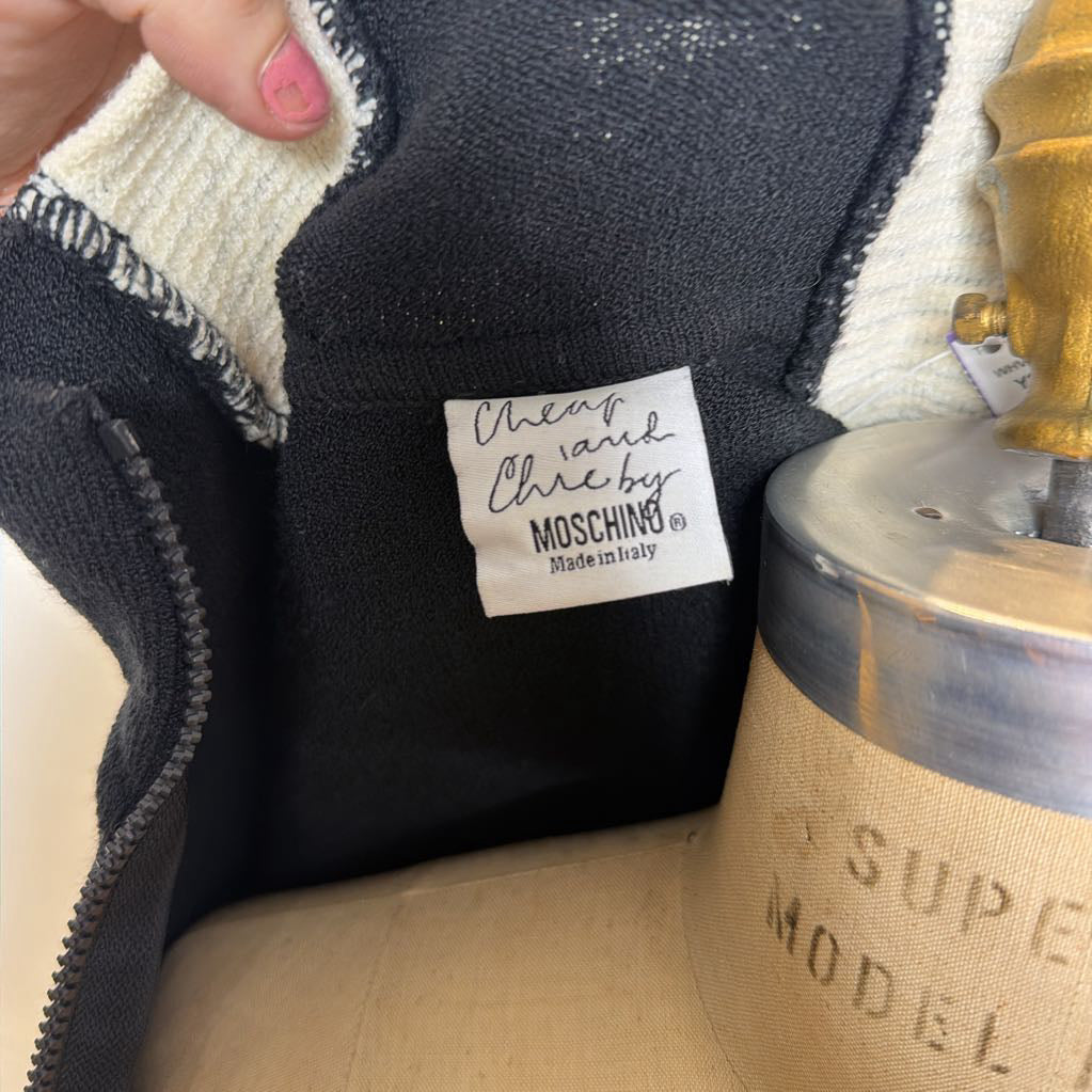 A hand holding a Moschino brand tag in a shirt. 