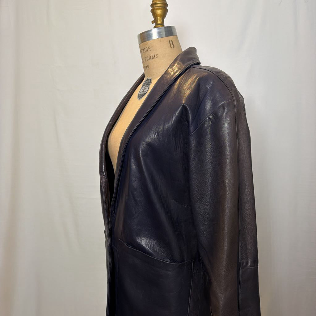 A navy leather trench jacket on a mannequin in front of a white wall. 