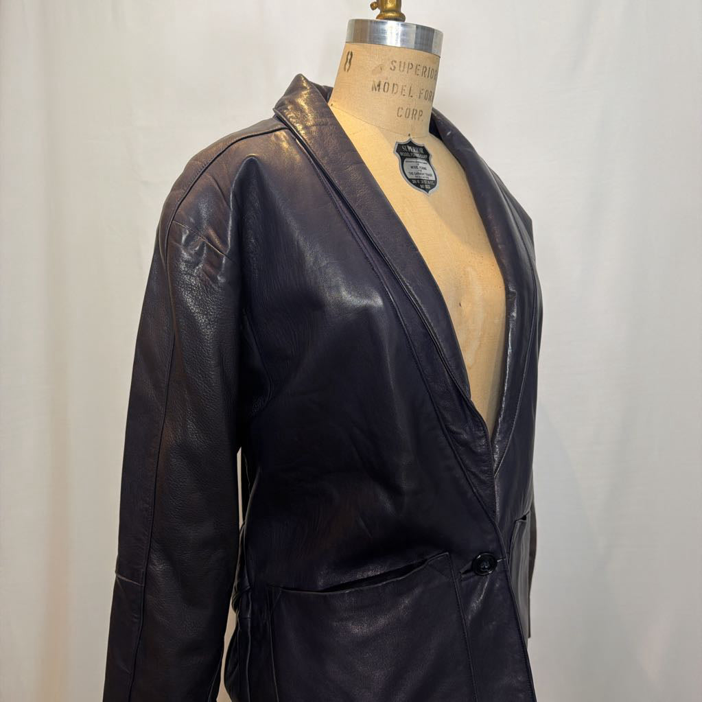 A navy leather trench jacket on a mannequin in front of a white wall. 
