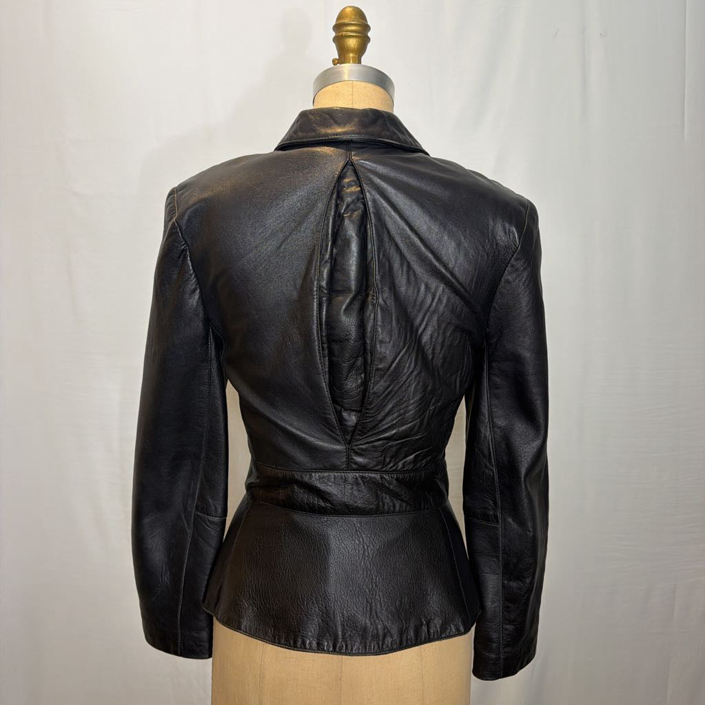A black leather jacket with an open spine pocket on the back on a mannequin in front of a white wall.