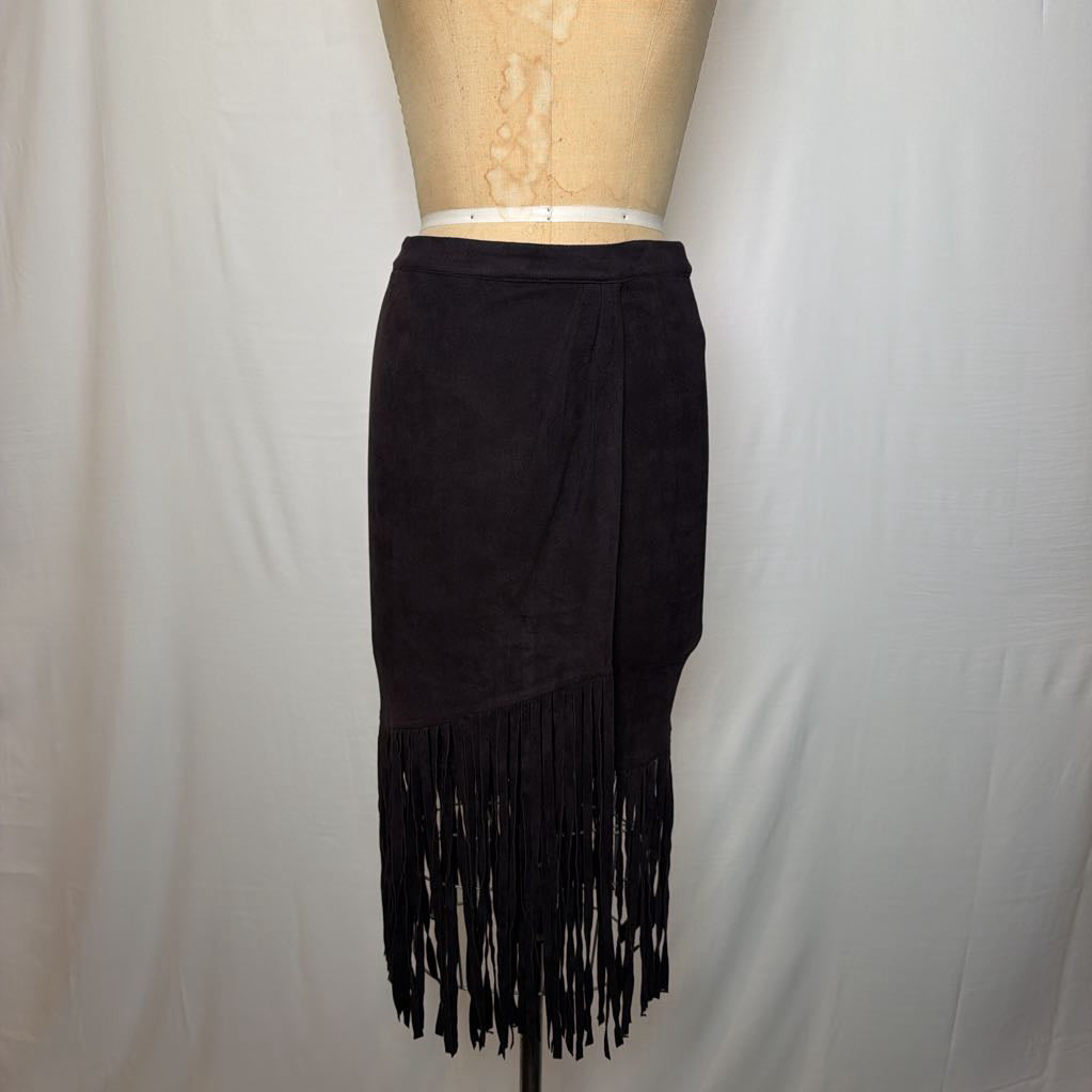 A black high-waisted skirt with a long fringe hem on a mannequin in front of a white wall. 