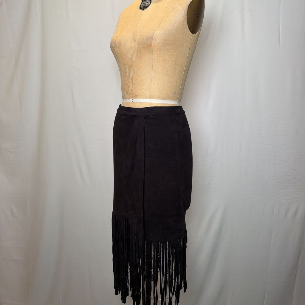 A black high-waisted skirt with a long fringe hem on a mannequin in front of a white wall. 