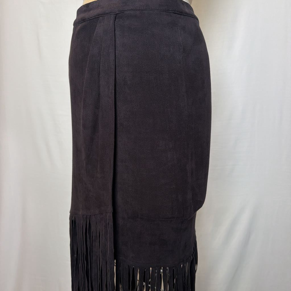 A black high-waisted skirt with a long fringe hem on a mannequin in front of a white wall. 
