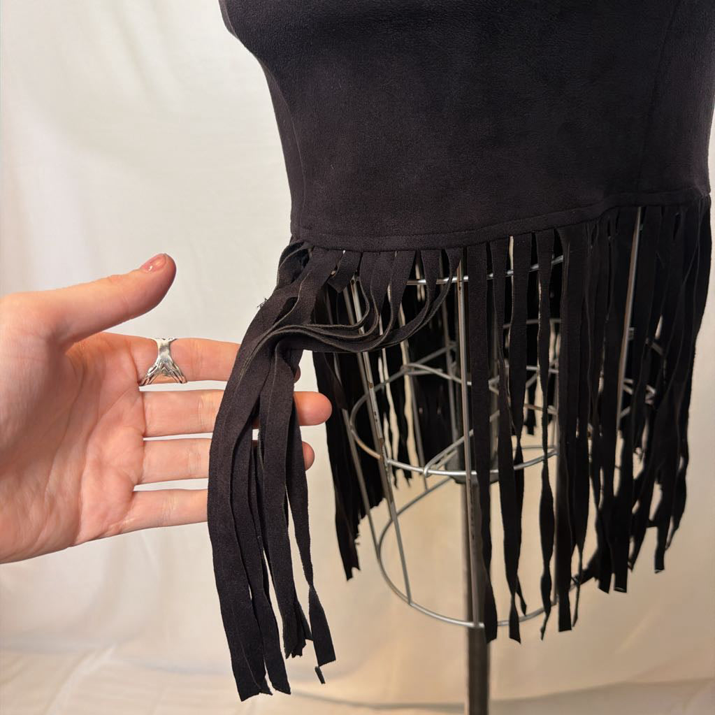 A black high-waisted skirt with a long fringe hem on a mannequin in front of a white wall. 