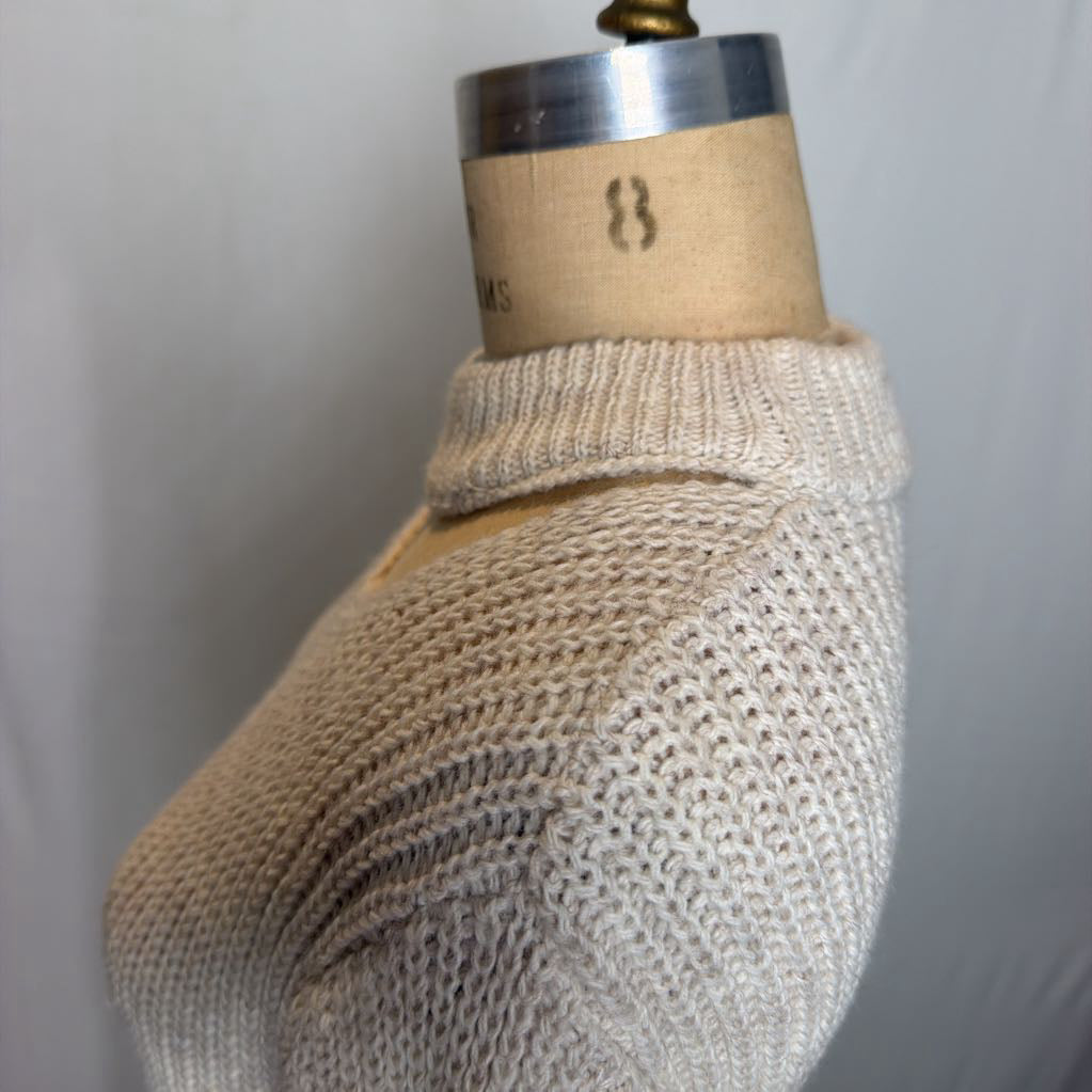 A white knit dress with an open neck and a slit on the bottom. It's on a mannequin in front of a white wall.