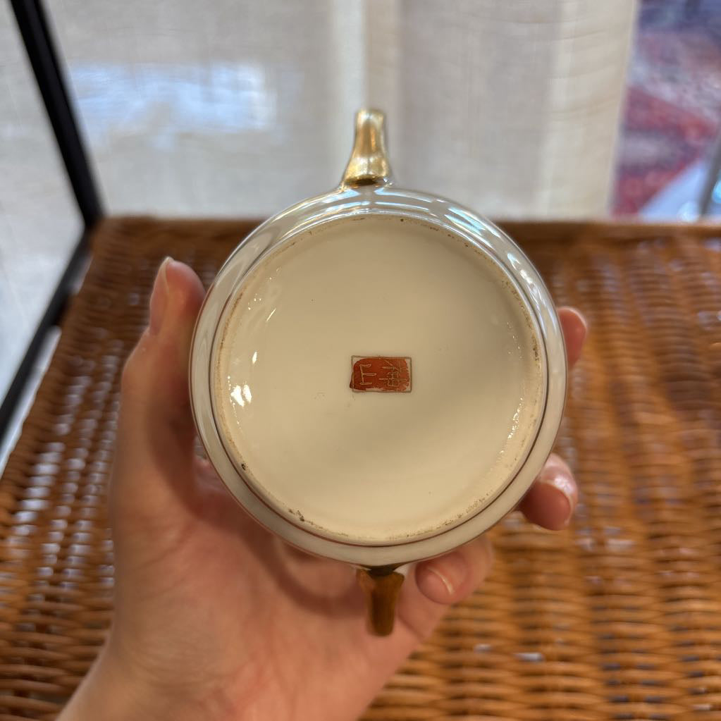 A ceramic bowl held by a hand over a rattan self to show the sticker at the bottom in a room setting. 