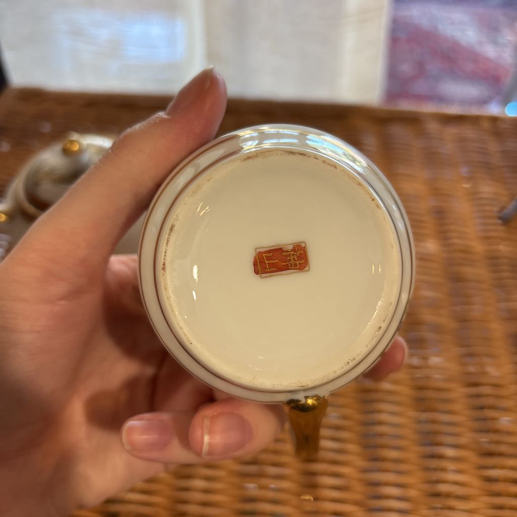 A ceramic bowl held by a hand over a rattan self to show the sticker at the bottom in a room setting. 