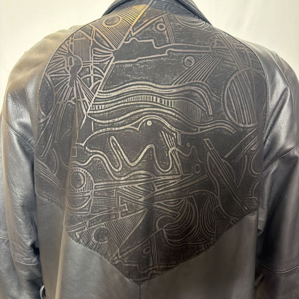 A black leather trench coat with wide shoulders and an abstract design on the back. Its on a mannequin in front of a white wall. 
