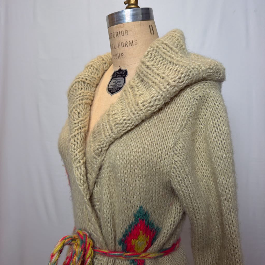 A tan belted knit sweater hoodie on a mannequin in front of a white wall.