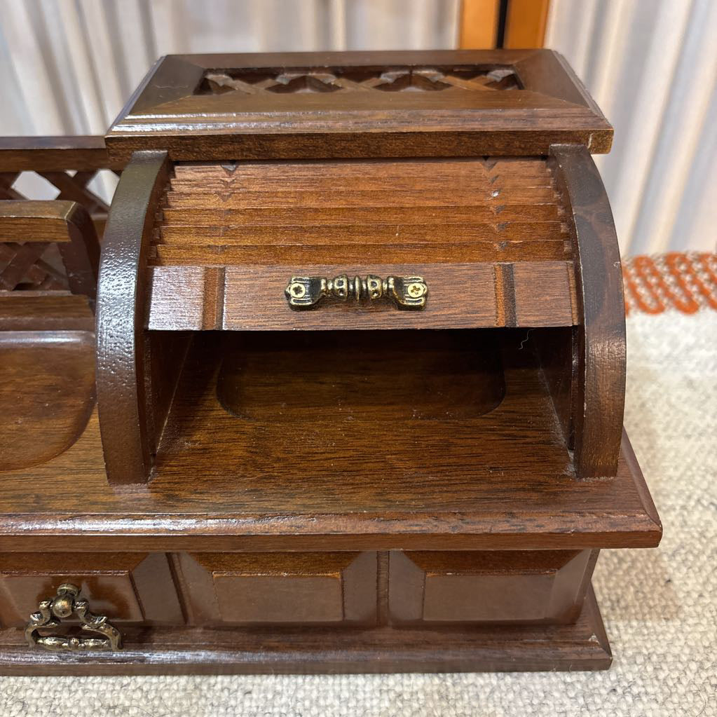 A wooden jewelry box/valet box on a woven runner in front of a white screen with part of a yellow painting showing.