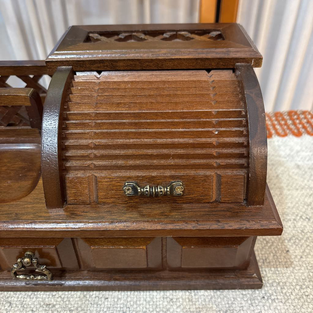 A wooden jewelry box/valet box on a woven runner in front of a white screen with part of a yellow painting showing.